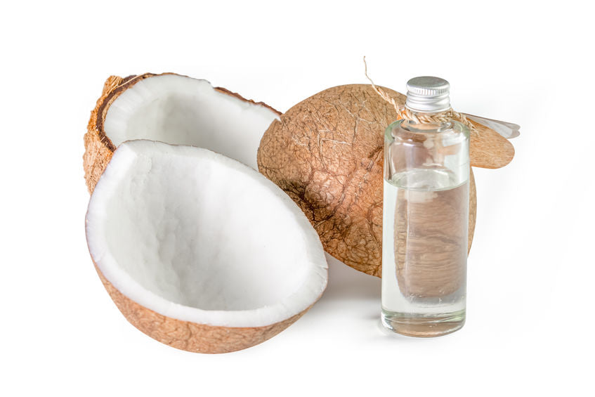 A bottle of fractionated coconut oil, with a whole coconut and a half coconut showing the inside. The oil is clear and light-colored.